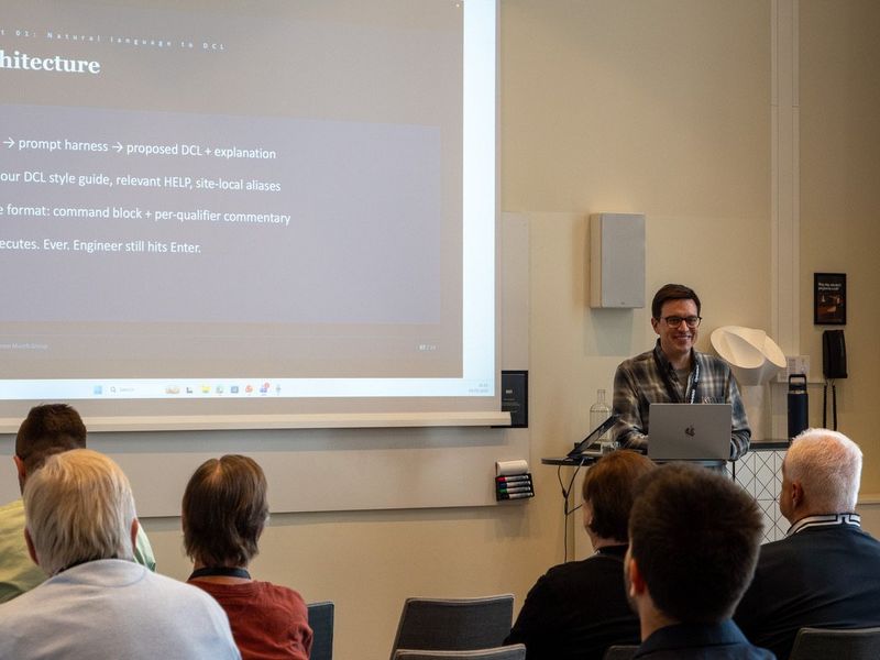 Dušan Dželebdžić presenting to a room at OpenVMS Bootcamp, a slide about turning natural language into DCL behind him